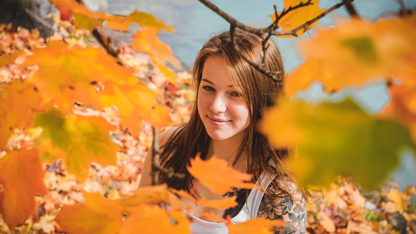 Portrait einer Frau zwischen gelben und orangefarbenen Herbstblättern