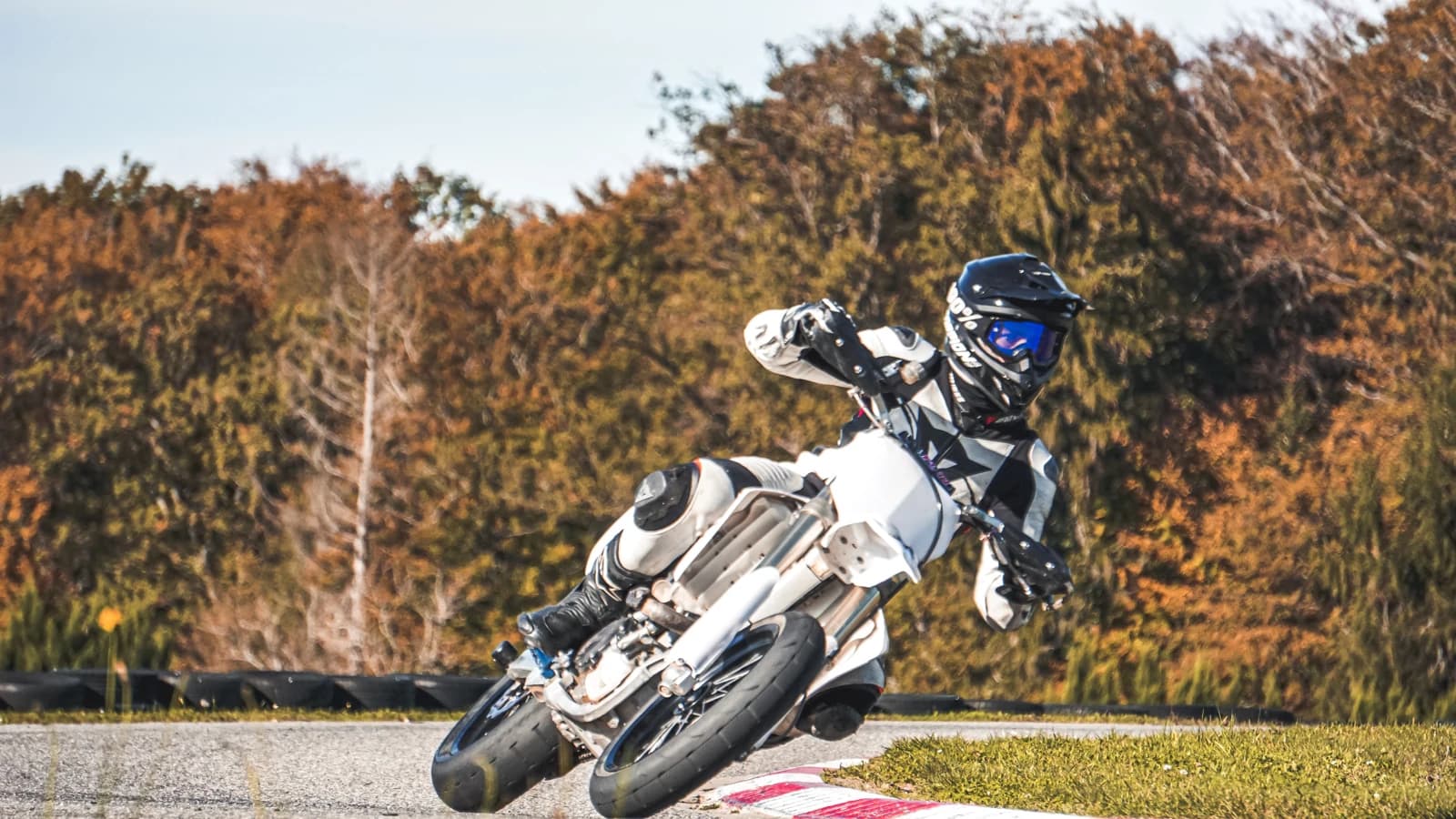 Supermoto-Fahrer in Schräglage auf einer Rennstrecke vor herbstlichen Bäumen