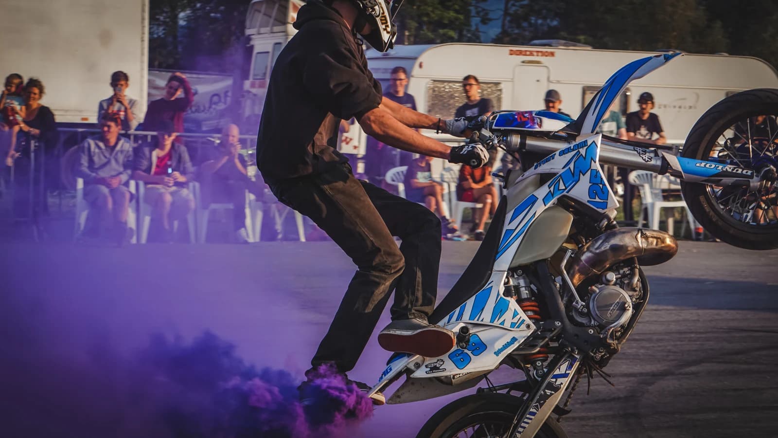 Motorrad-Stuntshow mit violettem Rauch und Publikum im Hintergrund