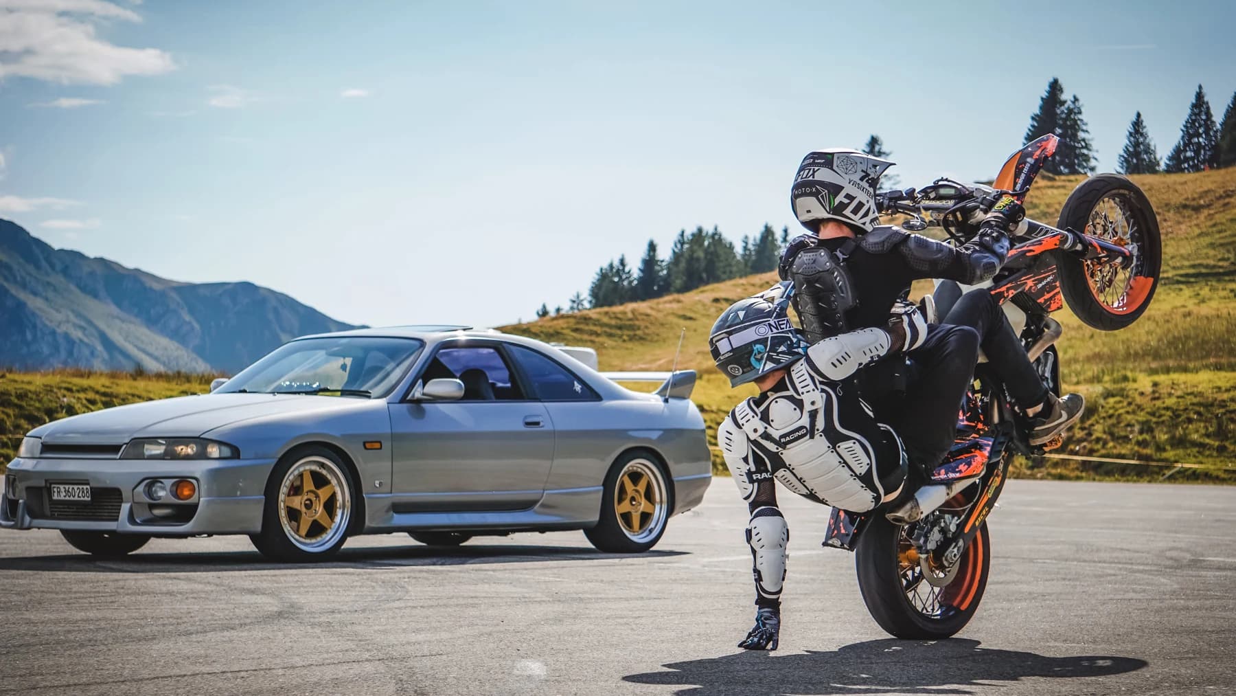 Silberner Sportwagen und Motorradfahrer auf dem Hinterrad auf einem Bergpass