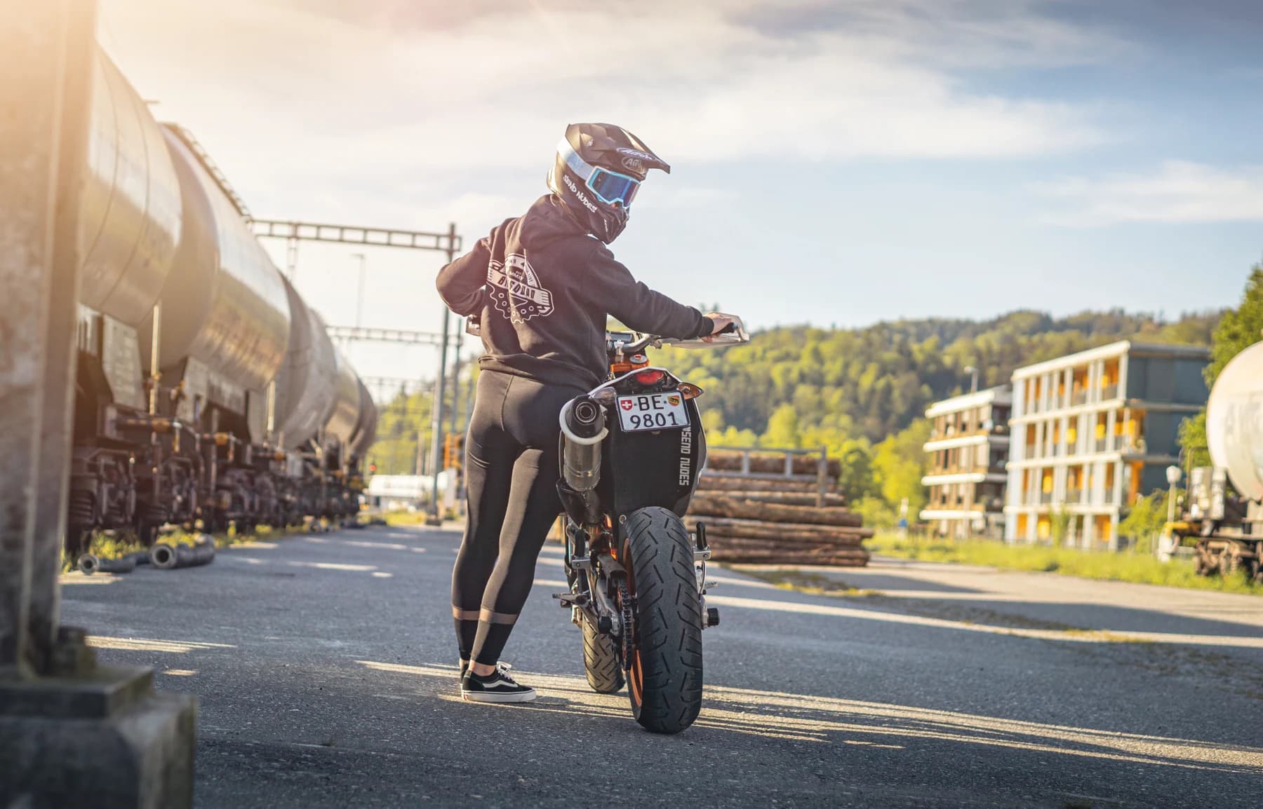 Motorradfahrer neben seiner Maschine im Gegenlicht vor Industriegebäuden